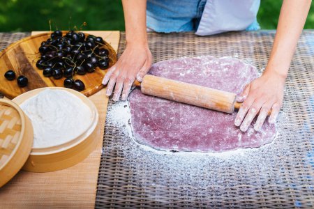Photo for A person is using a rolling pin to roll out dough on a hardwood table, preparing a delicious recipe. The wooden surface is stained and the fingers are pressing firmly.Mochi asian dessert - Royalty Free Image