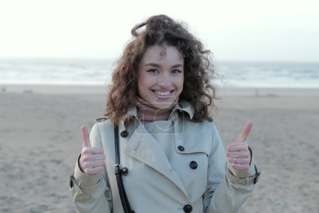 Foto de Mujer feliz dando un pulgar hacia arriba mientras está de pie en una playa - Imagen libre de derechos