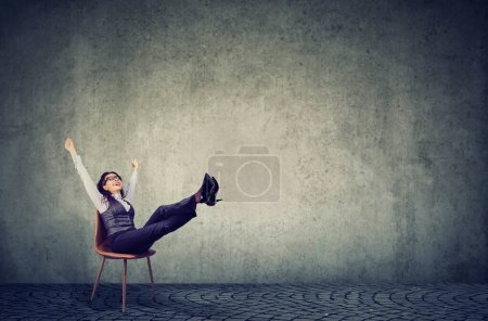 Téléchargez les photos : Jeune femme d'affaires heureuse dans la chaise de bureau avec les mains levées et les pieds levés - en image libre de droit