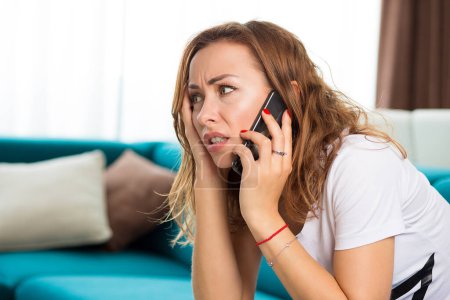 Photo for Portrait of an unhappy woman talking on cellphone in her apartment - Royalty Free Image