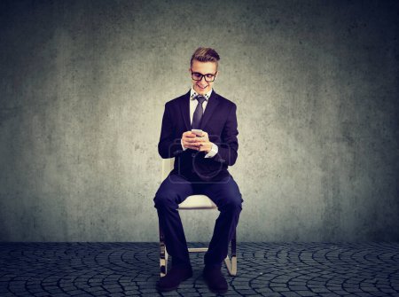 Smiling businessman sitting on a chair uses his mobile phone 
