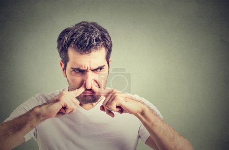 Young man wearing casual white t shirt smelling something stinky and disgusting, intolerable smell, holding breath with fingers on nose