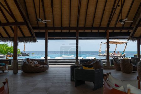 Foto de Fushifaru, Maldivas - 5 de mayo de 2022: Hermosas vistas de la piscina infinita y la playa en un día brillante desde el bar Fanihandhi en el lujoso complejo Fushifaru en el atolón de Lhaviyani. - Imagen libre de derechos