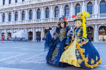Photo for Venice, Italy - March 01, 2022: Couple dressed in traditional costumes stand in front of the Ducal palace, part of the Venice Mask Carnival, Veneto, Italy - Royalty Free Image