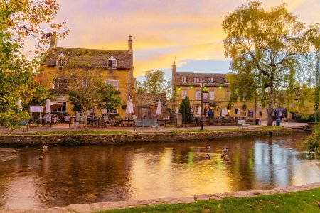 Photo for Bourton-on-the-Water, UK - October 17, 2022: Sunset scene of typical houses, the river Windrush, locals and visitors, in the village Bourton-on-the-Water, the Cotswolds region, England, UK - Royalty Free Image