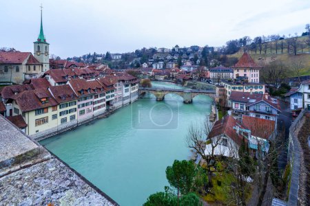 View of the Aare River, Nydeggkirche church, Untertorbrucke bridge, with various buildings, locals, and visitors, in Bern, Switzerland