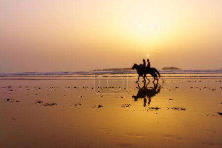 Foto de Vista del atardecer con silueta de caballos y jinetes en la playa de Essaouira (Mogador), Marruecos - Imagen libre de derechos