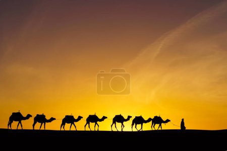 Photo for Sunrise silhouette of camels and handler, in the sand dunes of Merzouga, the Sahara Desert, Morocco - Royalty Free Image