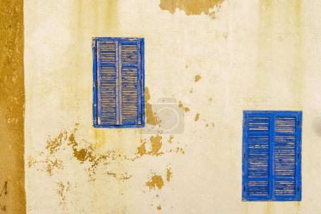 Téléchargez les photos : Vue des fenêtres et volets bleus sur un vieux mur de la maison avec peinture blanche. Essaouira (Mogador), Maroc - en image libre de droit