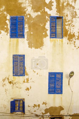 Téléchargez les photos : Vue des fenêtres et volets bleus sur un vieux mur de la maison avec peinture blanche. Essaouira (Mogador), Maroc - en image libre de droit