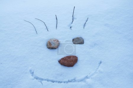 Ein fröhliches Gesicht auf Schnee gezeichnet mit Augen aus Steinen, die eine skurrile Winterszene schaffen