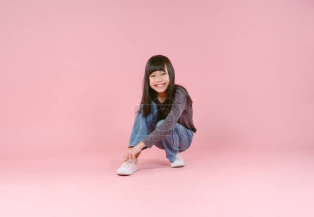 Nettes kleines asiatisches Mädchen sitzt auf dem Boden und legt ihre Schuhe isoliert in rosa Hintergrund