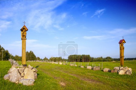 A village road through meadows to the church surrounded by stones, roadside chapels as a religious symbol