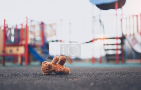 Téléchargez les photos : Lost teddy bear toy lying don on playground floor in gloomy day,Lonely and sad brown bear doll lied down alone in the park,lost toy or Loneliness concept,International missing Children day - en image libre de droit