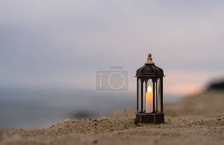 Téléchargez les photos : Lanterne islamique sur roche avec fond de plage de mer flou. Lampes traditionnelles décoratives de l'Aïd illuminées prêtes pour la saison sainte du Ramadan Kareem, Aïd Al fitr, Aïd al Adha, Aïd Moubarak, Mouharram - en image libre de droit