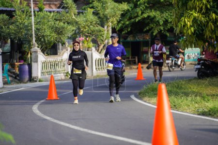 Foto de Los participantes o corredores de la Maratón de Jogja 42K, pasan una hermosa ruta alrededor del pueblo templo de Prambanan. : Yogyakarta, Indonesia - 18 de junio de 2023 - Imagen libre de derechos