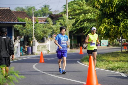 Foto de Los participantes o corredores de la Maratón de Jogja 42K, pasan una hermosa ruta alrededor del pueblo templo de Prambanan. : Yogyakarta, Indonesia - 18 de junio de 2023 - Imagen libre de derechos