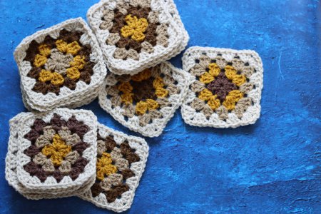 Téléchargez les photos : Granny carrés au crochet en laine naturelle brune, moutarde et beige. Doux et moelleux ornement au crochet sur fond texturé bleu. - en image libre de droit