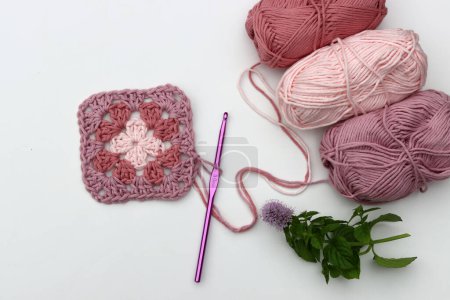 Rosa gehäkelte Granny Square, weiche Baumwollgarnknäuel in verschiedenen rosafarbenen Farbtönen. Weißer Hintergrund mit Kopierraum. Frühlingshäkelkonzept. 