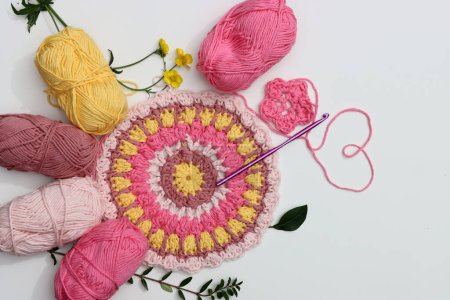 Téléchargez les photos : Mandala rose et jaune au crochet sur fond blanc avec espace de copie. Photo de vue du dessus de boules de fil de coton, crochet et fleurs. Elément décoratif fait main. - en image libre de droit