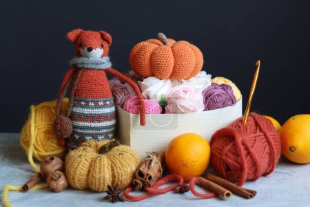Renard jouet tricoté, boules de fil et décorations d'automne sur un fond gris avec espace pour le texte. Jouet amigurumi mignon. 
