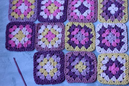 Handmade crocheting. Crocheted pink, purple, yellow and white granny squares. Cute pattern close up photo. Soft cotton yarn texture. Grey background with space for text. 