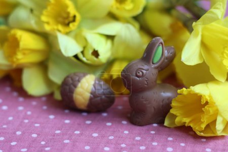 Conejitos de chocolate de Pascua y narcisos sobre mantel rosa. Tarjeta de Pascua brillante y colorida.