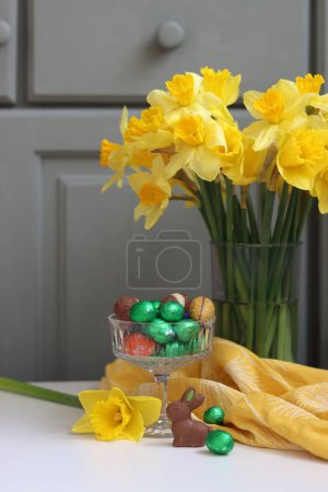 Bouquet of golden daffodils in a glass vase on green wooden background with space for text. 