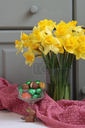 Bouquet of golden daffodils in a glass vase on green wooden background with space for text. 
