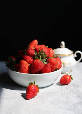 Erdbeeren in einer Schüssel auf einer weißen Tischdecke vor schwarzem Hintergrund mit Platz für Text. 