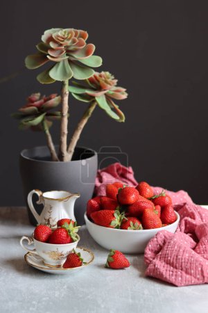 Tasse Tee mit Erdbeeren und saftigen Pflanzen auf dunklem Hintergrund mit Platz für Text. Frisches Konzept. 