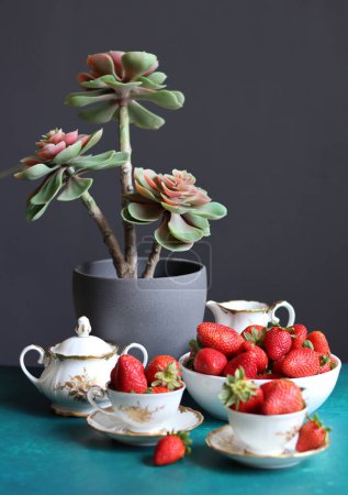 Taza de té con fresas y planta suculenta sobre fondo oscuro con espacio para el texto. Comer concepto fresco. 