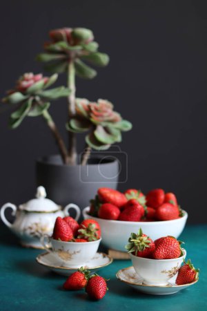 Tasse Tee mit Erdbeeren und saftigen Pflanzen auf dunklem Hintergrund mit Platz für Text. Frisches Konzept. 