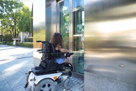 Foto de Mujer discapacitada con movilidad reducida y pequeña estatura en una silla de ruedas eléctrica tratando de entrar en un ascensor. Discapacidad conceptual, discapacidad, incapacidad, necesidades especiales, barreras arquitectónicas. - Imagen libre de derechos