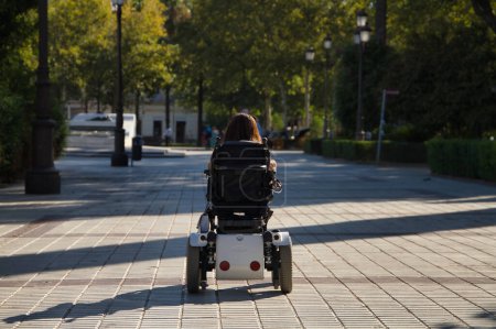Mujer con discapacidad, movilidad reducida y baja estatura en silla de ruedas eléctrica caminando por el centro de la ciudad, vista desde atrás. Concepto discapacidad, discapacidad, incapacidad, necesidades especiales.