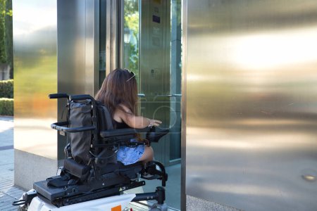 Foto de Mujer discapacitada con movilidad reducida y pequeña estatura en una silla de ruedas eléctrica tratando de entrar en un ascensor. Discapacidad conceptual, discapacidad, incapacidad, necesidades especiales, barreras arquitectónicas. - Imagen libre de derechos