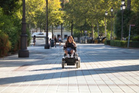 Foto de Mujer discapacitada con movilidad reducida y pequeña estatura en una silla de ruedas eléctrica caminando por el centro de la ciudad. Discapacidad conceptual, discapacidad, incapacidad, necesidades especiales, barreras arquitectónicas. - Imagen libre de derechos