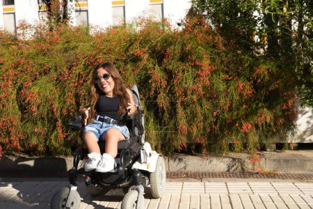 Foto de Mujer discapacitada con movilidad reducida y pequeña estatura en una silla de ruedas eléctrica posando felizmente en la calle en un día soleado. Concepto discapacidad, discapacidad, incapacidad, necesidades especiales. - Imagen libre de derechos