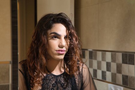 Téléchargez les photos : Young transgender girl, looking at herself in the mirror after having make up, with serious and worried gesture. Concept transgender, lgtbi, homosexuality, gay, diversity. - en image libre de droit
