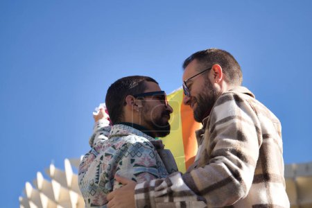 Photo for Real marriage of gay couple, looking at each other while holding a gay pride flag, happy and complicit. Concept lgtb, lgtbiq+, couples, in love, pride, flag. - Royalty Free Image