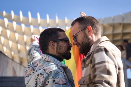 Photo for Real marriage of gay couple, looking at each other while holding a gay pride flag, happy and complicit. Concept lgtb, lgtbiq+, couples, in love, pride, flag. - Royalty Free Image