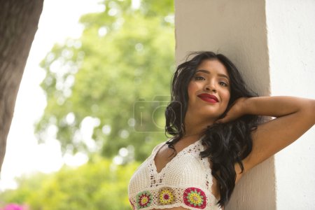 Femme sud-américaine, jeune, belle, brune, avec haut au crochet et jeans appuyés sur une colonne, avec un regard tendre et rêveur. Concept de beauté, mode, tendance, ethnicité, diversité.