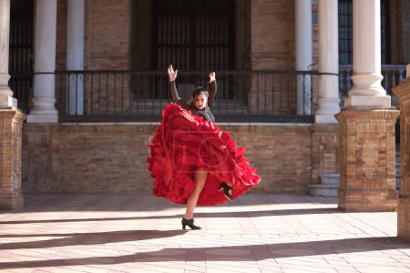 Junge, schöne, brünette Frau in schwarzem Hemd und rotem Rock, die zwischen Marmorsäulen auf dem spanischen Platz in Sevilla Flamenco tanzt. Flamenco-Konzept, Tanz, Kunst, typisch spanisch.