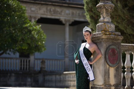 Photo for Young, pretty, blonde woman in green party dress with sequins, diamond crown and beauty pageant winner's sash, calm and relaxed leaning on a column. Concept of beauty, fashion, pageant, model. - Royalty Free Image