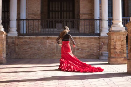 Junge, schöne, brünette Frau in schwarzem Hemd und rotem Rock, die zwischen Marmorsäulen auf dem spanischen Platz in Sevilla Flamenco tanzt. Flamenco-Konzept, Tanz, Kunst, typisch spanisch.