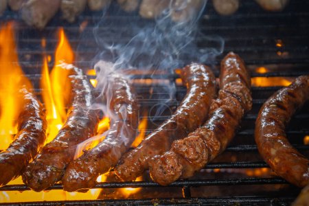 merguez cooking on a barbecue grill, with flames fanned by the fat.