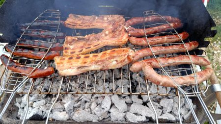 sausages, slices of bacon and merguez cooking on a barbecue