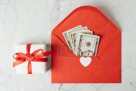 Photo for Red paper envelope with money dollars bills. Flat lay of gray working table background with Valentine gift, letter, heart shape. Top view, mock up greeting card. Valentines Day budget - Royalty Free Image