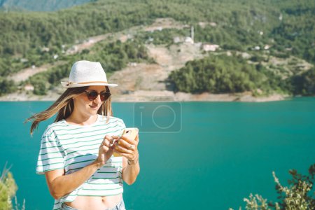 Photo for Woman texting online on mobile phone of mountains lake background. Traveler female chat messages on cellphone on the blue lake outdoors travel adventure vacation. Using smartphone - Royalty Free Image