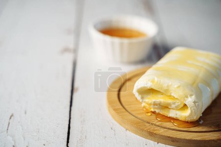 Close up picture of white cream milky kaymak butter roll poured with honey on wooden plate.